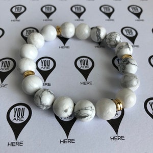 Peut inclure: Bracelet en perles de pierre blanches et grises avec des accents dor&eacute;s. Le bracelet est compos&eacute; de perles rondes et a un design simple.
