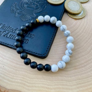 May include: A black and white beaded bracelet with a gold clasp. The bracelet is made of round beads, with half of the beads being black and the other half being white.