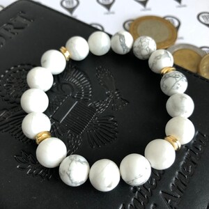 Peut inclure: Bracelet en perles d'howlite blanche avec des accents dor&eacute;s. Le bracelet est compos&eacute; de perles rondes et a un design simple.