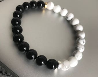 Puede incluir: Un brazalete de cuentas negras y blancas con un acento dorado. El brazalete está hecho de cuentas de ónix negro y howlite blanca.