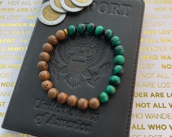 May include: A black leather passport holder with the words "United States of America" embossed on the front. A green and brown beaded bracelet is resting on top of the passport holder. The bracelet has a gold accent.