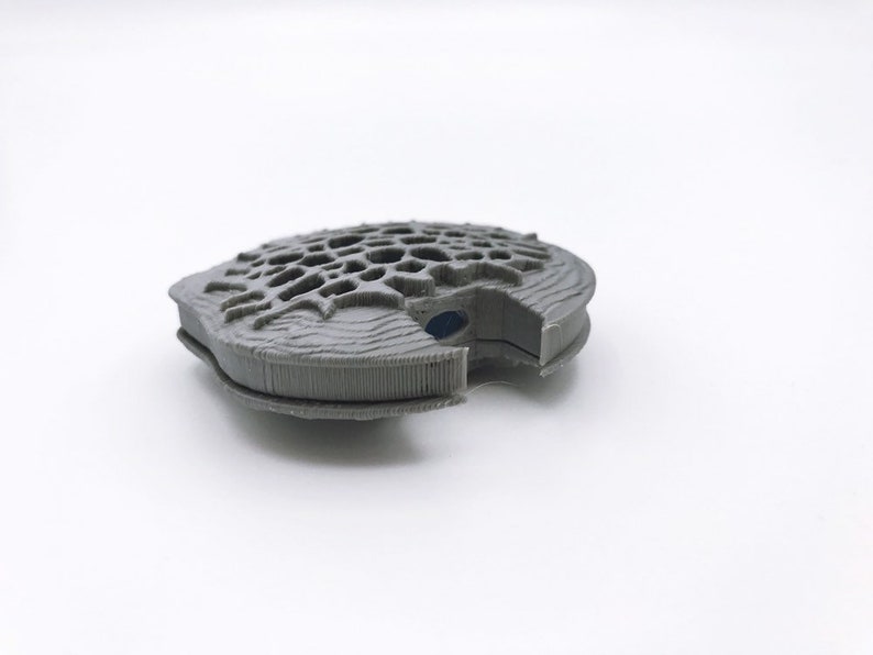 May include: A gray 3D printed object with a geometric design. The object is open and has a small blue piece inside.