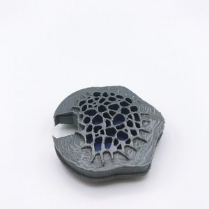 May include: A gray 3D printed object with a detailed, intricate design. The object has a honeycomb-like pattern with a blue center.