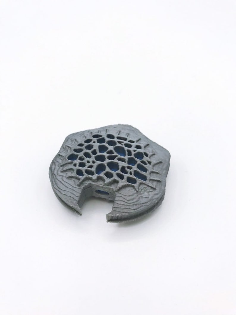 May include: A gray 3D printed object with a geometric design and a hole in the center. The object has a textured surface and a blue interior.