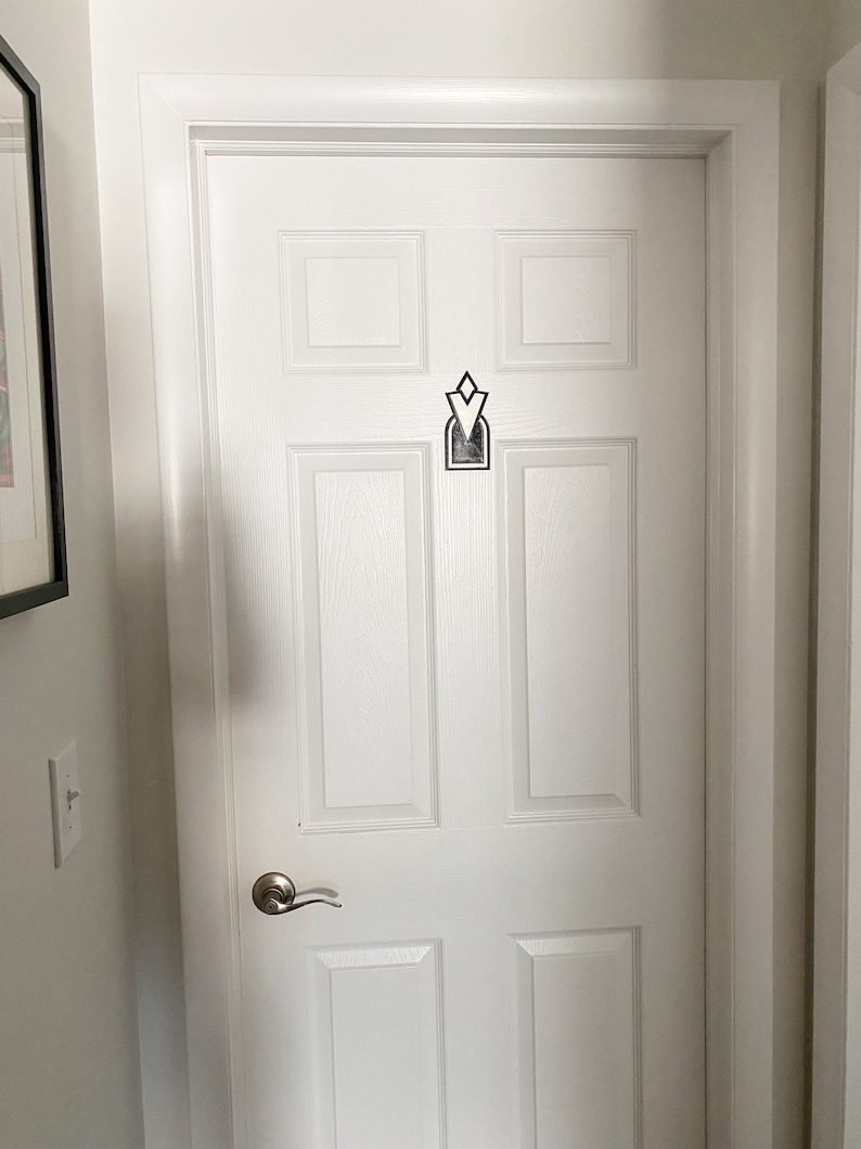 Pu&ograve; includere: Una porta bianca con una maniglia argentata e un design geometrico bianco e nero sul pannello centrale.