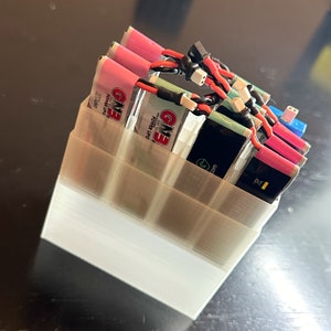 May include: A white plastic battery storage organizer with six compartments holding multiple colorful lithium polymer batteries. The batteries have black wires and are labeled "GMB Power Up".