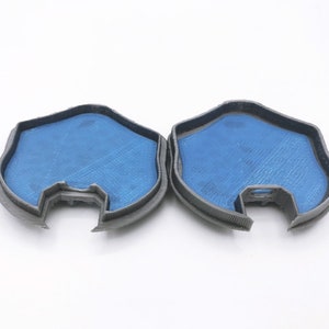 May include: Two gray 3D printed molds with a blue interior. The molds are shaped like a rounded rectangle with a cutout on one side.