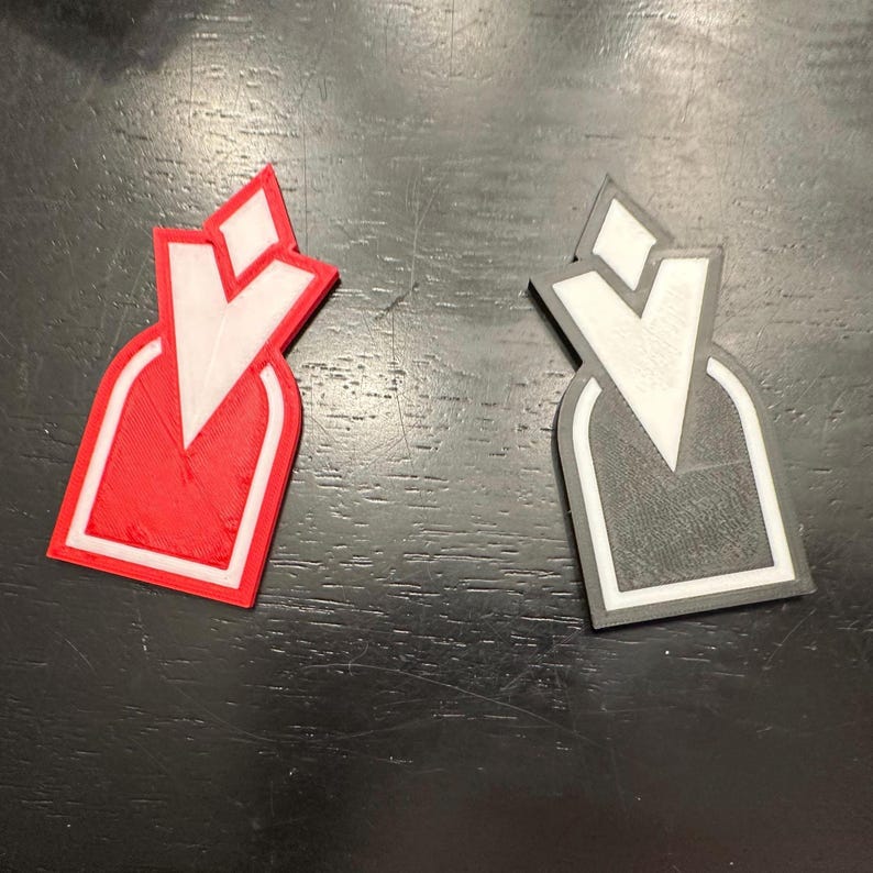 Pu&ograve; includere: Due tappi per bottiglia stampati in 3D, uno rosso e uno nero, con un design bianco a forma di V stilizzata.