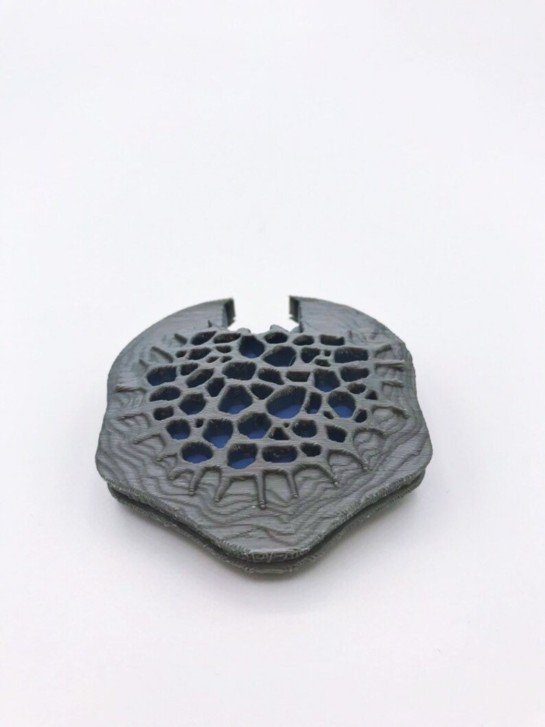 May include: A 3D printed, gray, geometric design with a blue center. The design is intricate and has a textured surface.