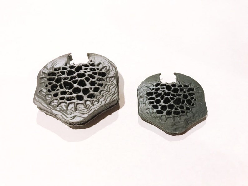 May include: Two gray 3D printed objects with a honeycomb pattern. The objects are different sizes and are on a white background.