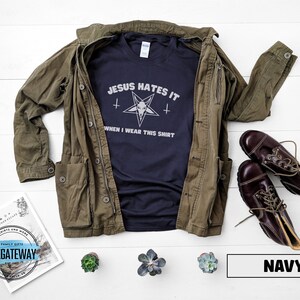May include: A navy blue t-shirt with the text "Jesus Hates It" and a pentagram with a goat's head inside. The text below the pentagram reads "When I Wear This Shirt".