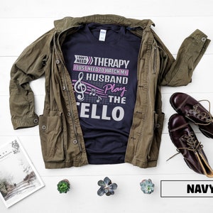 Pu&ograve; includere: Maglietta blu navy con un grafico di nota musicale e il testo "Non ho bisogno di terapia, ho solo bisogno di guardare mio marito suonare il violoncello".