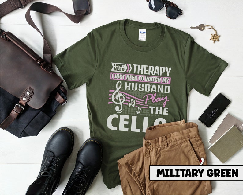 Pu&ograve; includere: Una maglietta verde con il testo "I don't need therapy I just need to watch my husband play the cello" in lettere bianche e rosa. Il testo &egrave; accompagnato da una nota musicale e note musicali.