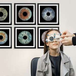 May include: Six framed prints of eye irises in black frames with white mounts. The irises show diverse colours and patterns. A young person wears an eye exam device while an optometrist adjusts it.