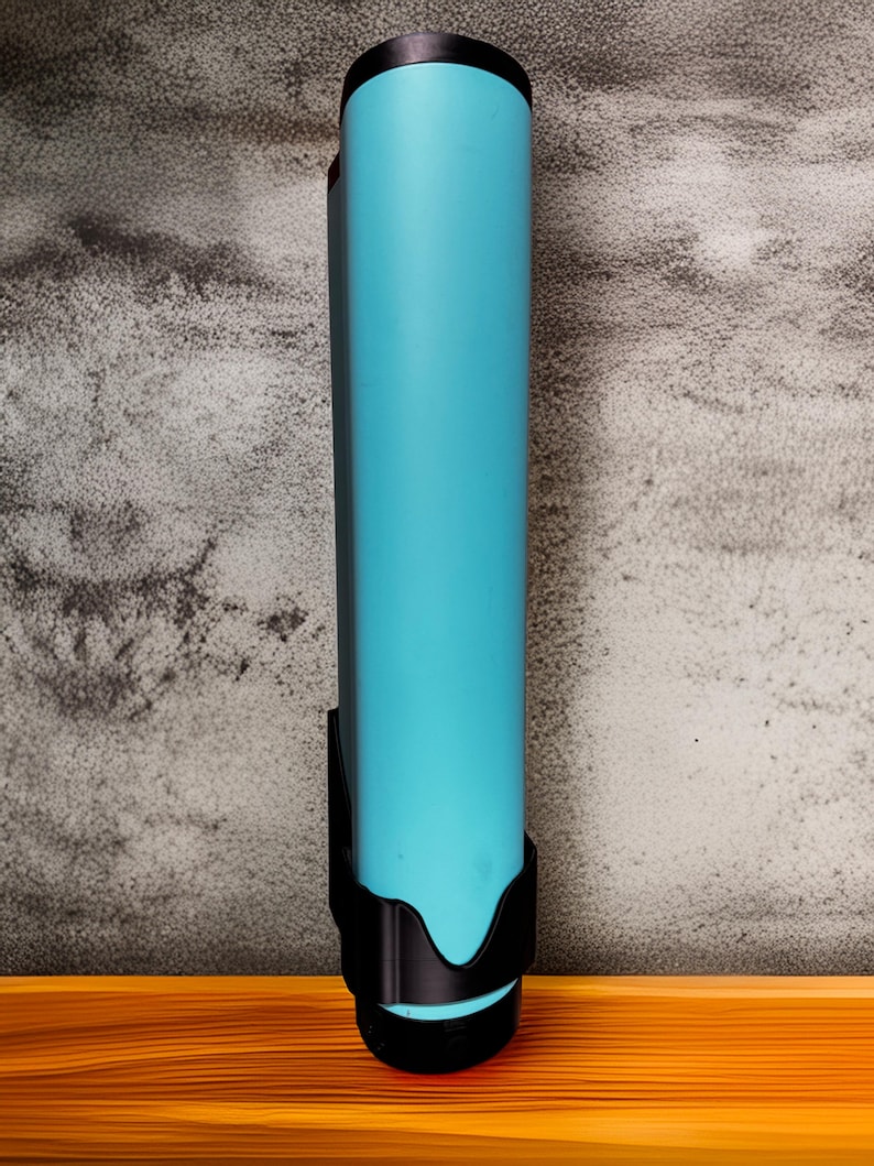 Op de afbeelding: Een lange, cilindrische waterfles in een levendige turquoise kleur, met een zwarte dop en een zwarte houder. De fles staat tegen een getextureerde grijze muur en een houten oppervlak.