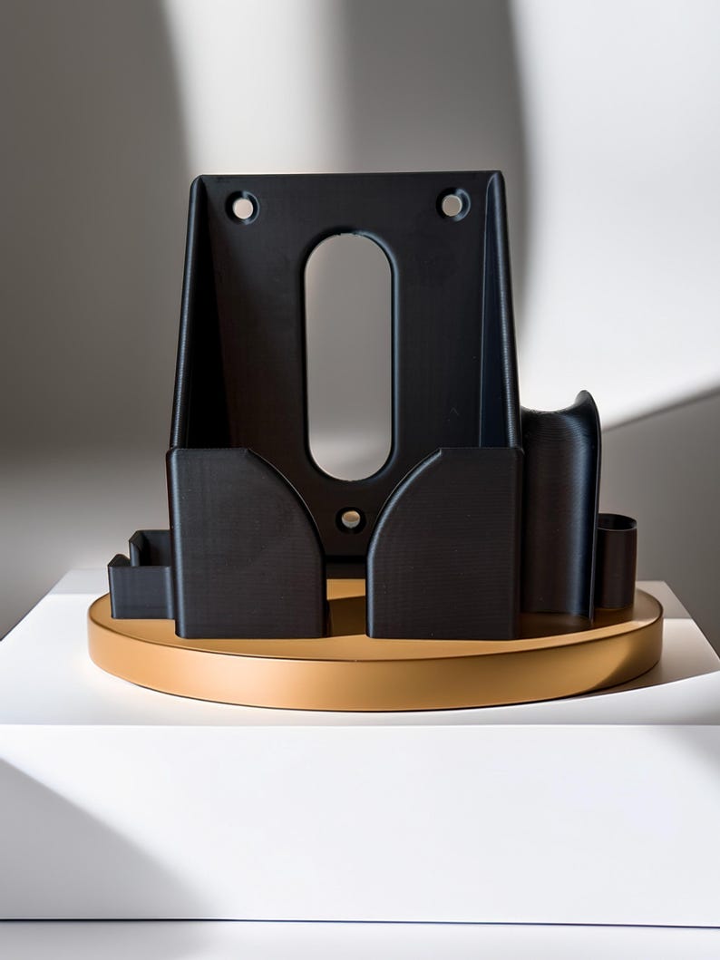 Pu&ograve; includere: Un oggetto geometrico nero con un ritaglio ovale e due fori nella parte superiore. Poggia su una base rotonda e marrone chiaro. L'oggetto ha diversi scomparti e un design curvo, con un'estetica minimalista.