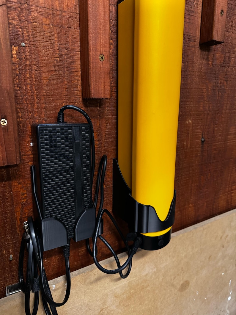 Op de afbeelding: Een gele laadstation met een zwarte basis en een zwarte voedingsadapter gemonteerd op een houten oppervlak. De voedingsadapter heeft een zwart snoer dat is aangesloten op een stopcontact.