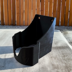 Op de afbeelding: Een zwarte plastic container met een gebogen voorkant en een platte achterkant. De container heeft een uitsparing aan de voorkant en twee gaten aan de bovenkant. De voorkant van de container heeft een decoratief pijldesign.