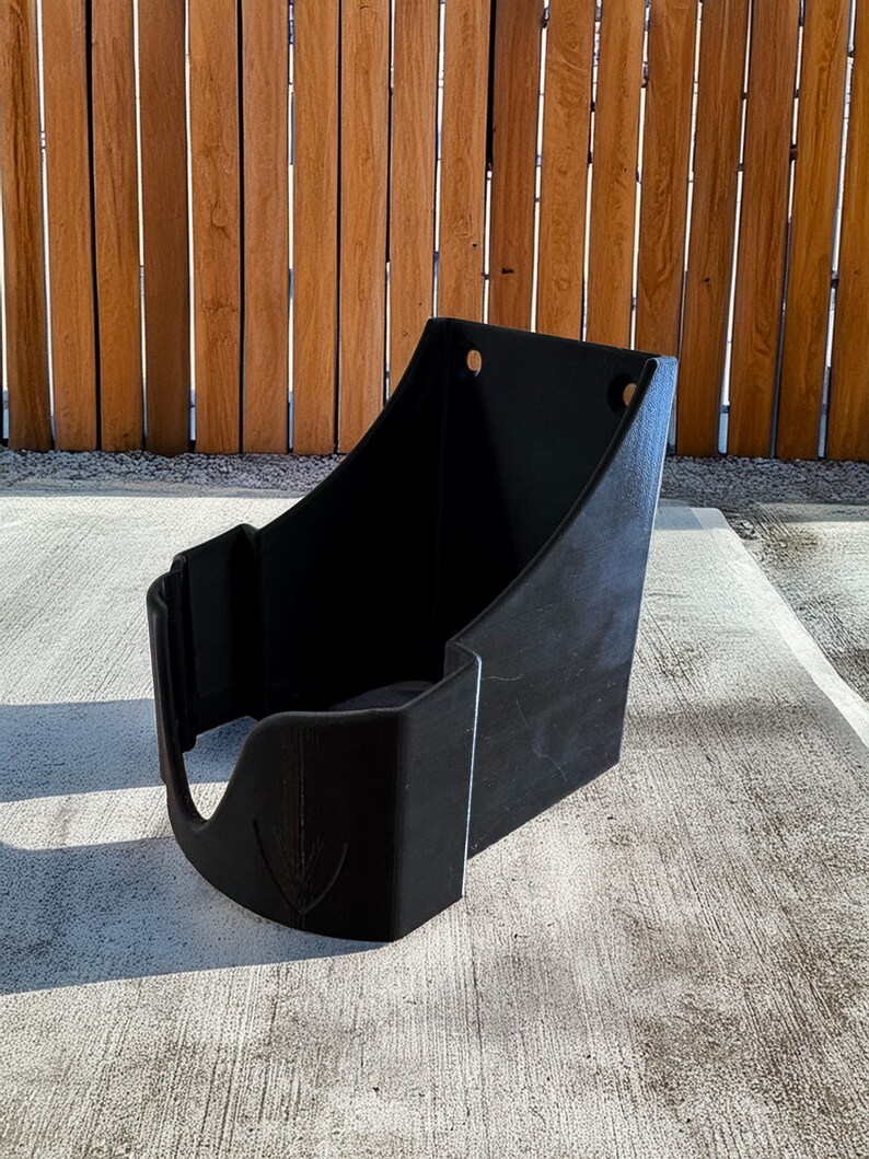 Op de afbeelding: Een zwarte plastic container met een gebogen voorkant en een platte achterkant. De container heeft een uitsparing aan de voorkant en twee gaten aan de bovenkant. De voorkant van de container heeft een decoratief pijldesign.