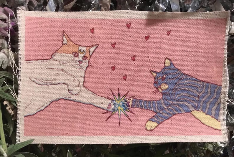 Op de afbeelding: Rechthoekige patch met twee gestileerde katten die hun poten aanraken, op een roze achtergrond. E&eacute;n kat is wit en oranje, de andere blauw met strepen. Kleine rode hartjes zweven. Een sterrenpatroon staat tussen hun poten.
