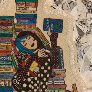 May include: A woman with blue hair is surrounded by a stack of books. She is holding a book that says "Don't Panic!" The woman is wearing a black and white polka dot dress.