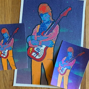 May include: Artwork featuring a stylized illustration of a musician playing a red and white electric guitar. The figure is depicted in shades of blue, pink, and orange against a starry purple background. The image is presented on canvas and smaller prints.