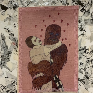May include: A rectangular patch with a pink background features a Star Wars-themed illustration. It depicts a Wookiee embracing a woman, with small red hearts floating above them. The patch has a pink stitched border.