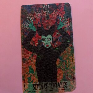 May include: A tarot card with a colorful, abstract background. The card depicts a figure with green skin and black hair wearing a black outfit. The card is labeled "VII" and "SEVEN OF PENTACLES".