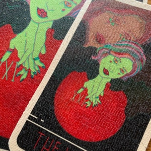 May include: Tarot card featuring a green-skinned figure with red lips and multi-colored hair. The figure is set against a red background with a black border. The text "THE WORLD" is visible at the bottom of the card.