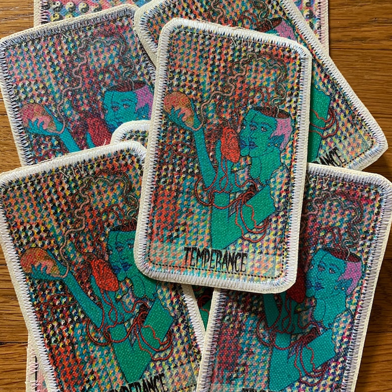 K&ouml;nnte beinhalten: Rechteckige Aufn&auml;her mit einem farbenfrohen, psychedelischen Design mit einer t&uuml;rkisfarbenen Figur mit dem Wort "TEMPERANCE". Die Aufn&auml;her haben einen wei&szlig;en Rand und sind auf einer Holzoberfl&auml;che verstreut.