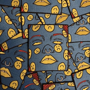 Puede incluir: Un conjunto de parches de tela azul con caras tristes amarillas, labios y detalles faciales. Los parches están dispuestos en un patrón en capas, algunos cuadrados y otros con bordes curvos. Se ven detalles en rojo.
