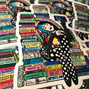 Może przedstawiać: Naklejka przedstawiająca fantazyjną ilustrację osoby z niebieskimi włosami, leżącej na stosie kolorowych książek. Osoba ma na sobie czarno-biały str&oacute;j w kropki. Widoczne są tytuły książek.