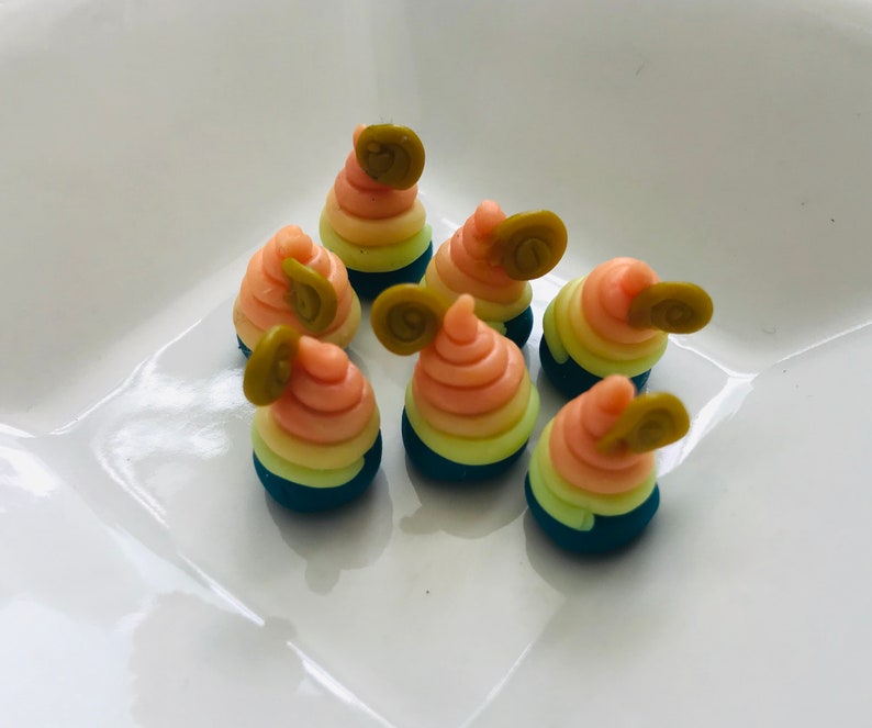 Pode incluir: Seis pequenos doces coloridos em forma de espiral com uma folha verde no topo. Os doces est&atilde;o dispostos em um prato branco.