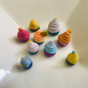 Pode incluir: Uma cole&ccedil;&atilde;o de dez mini cupcakes com cobertura colorida e granulado. Os cupcakes s&atilde;o feitos de argila polim&eacute;rica e est&atilde;o dispostos em um prato branco.