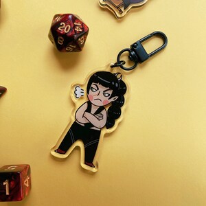 May include: A black and white cartoon character keychain with a black chain. The character is a woman with black hair and a white shirt. She is making a frustrated face and has a thought bubble above her head.