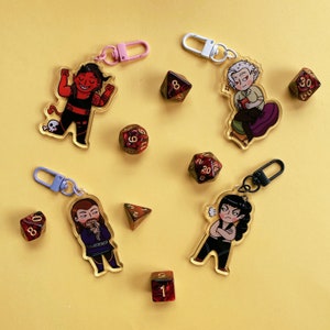 May include: A set of ten colorful keychains featuring cartoon characters and dice. The keychains are made of clear acrylic and have a variety of colors, including red, blue, green, yellow, and black. The characters are all different and include a devil, a wizard, a warrior, and a dragon. The dice are all different colors and have numbers on them.