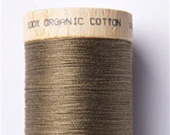 Könnte beinhalten: Eine Spule mit 100% Bio-Baumwollgarn in dunkelbrauner Farbe. Die Spule ist aus Holz und hat den Text "100% Organic Cotton" auf der Oberseite. Die Unterseite der Spule hat den Text "Made in"