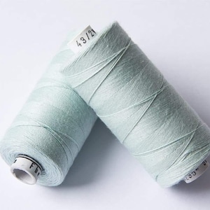 May include: Two spools of light blue sewing thread. The spools are labelled "43/2".