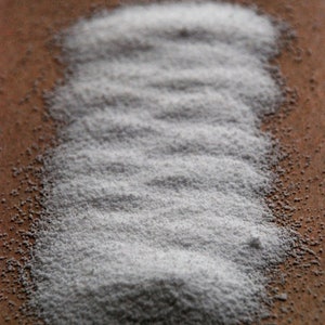 Op de afbeelding: Een close-up van een hoop wit poeder op een bruin oppervlak.