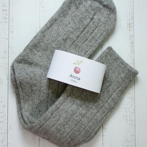 Brown unfolded long Anna wool sock with a white label on a white wooden rustic background