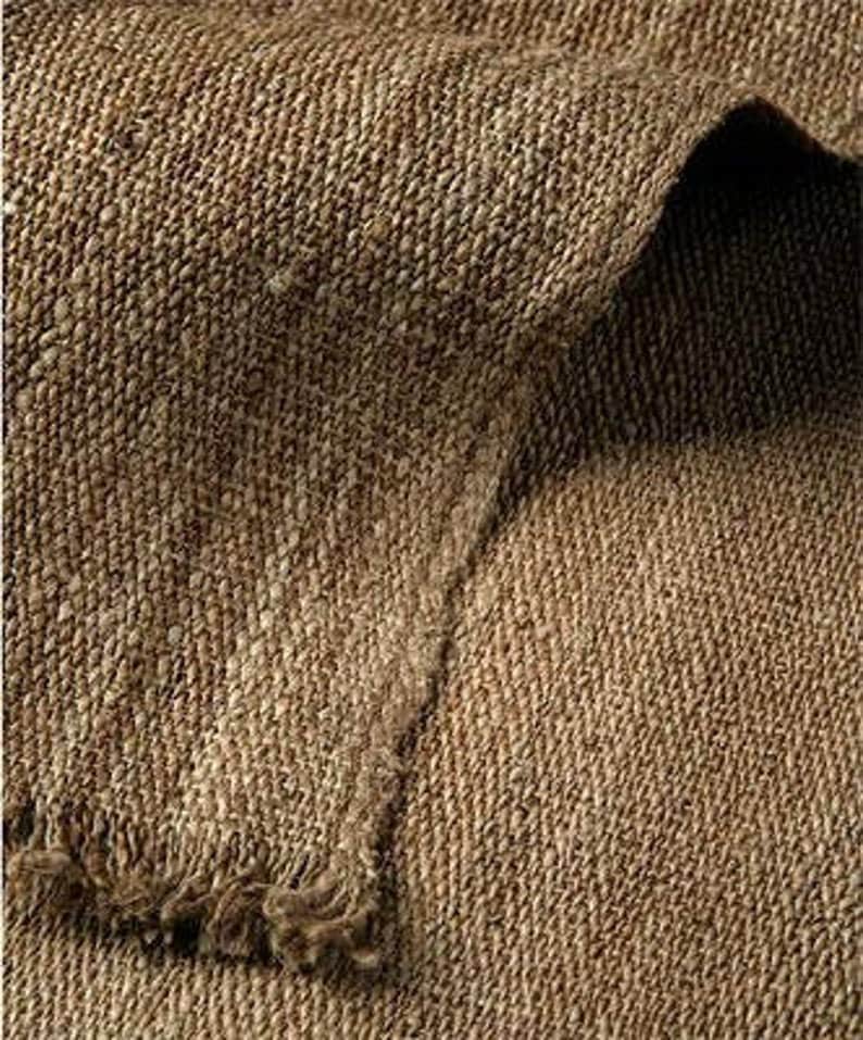 May include: Close-up of a brown woven fabric with a rough texture. The fabric has a subtle herringbone pattern and a frayed edge.