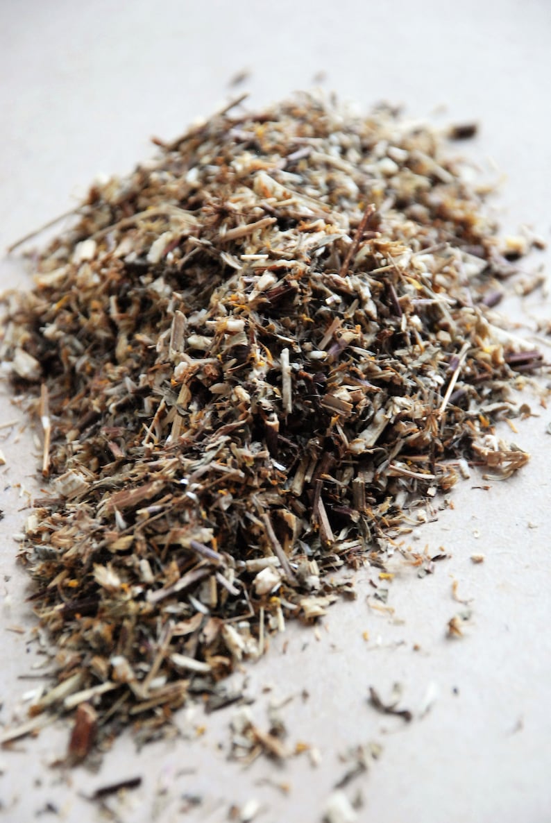 May include: A close-up of a pile of dried herbs, including brown stems, green leaves, and small yellow flowers.