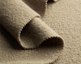 May include: Close-up of a folded section of tan-colored fabric. The fabric has a textured, fleecy appearance with a slightly uneven surface. The edges of the fabric are cut with a scalloped pattern. The overall look is soft and inviting.