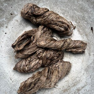 May include: Close-up of several twisted, brown fiber bundles. The fibers have a coarse texture and appear to be natural, possibly plant-based. The bundles are arranged on a light gray, textured surface.