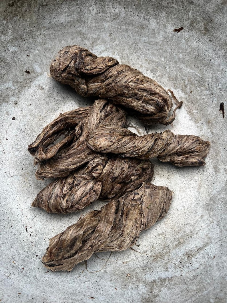 May include: Close-up of several twisted, brown fiber bundles. The fibers have a coarse texture and appear to be natural, possibly plant-based. The bundles are arranged on a light gray, textured surface.