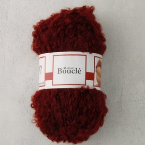 May include: A ball of deep red mohair boucle yarn with a white label that reads "Mohair Bouclé".
