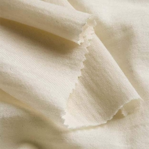 Puede incluir: Primer plano de una tela blanquecina doblada. La tela tiene un tejido texturizado y un borde en bruto sin terminar. El material parece suave y ligero, con sutiles variaciones de color.