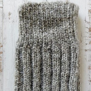 Wool sock cuff in grey brown on a white wooden surface.