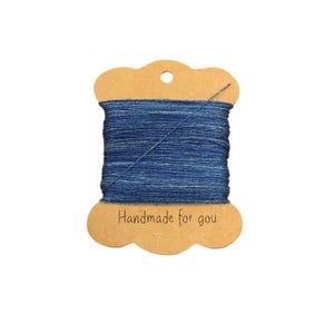 Op de afbeelding: Een spoel met blauwe en witte garen op een bruin kartonnen label met de tekst "Handmade for you".