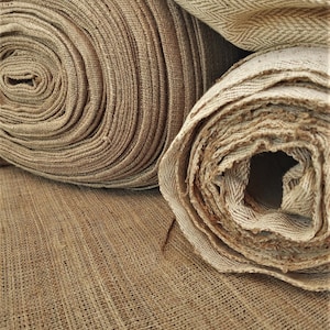 May include: Three rolls of brown burlap fabric, two are rolled up and one is unrolled. The fabric has a woven texture.